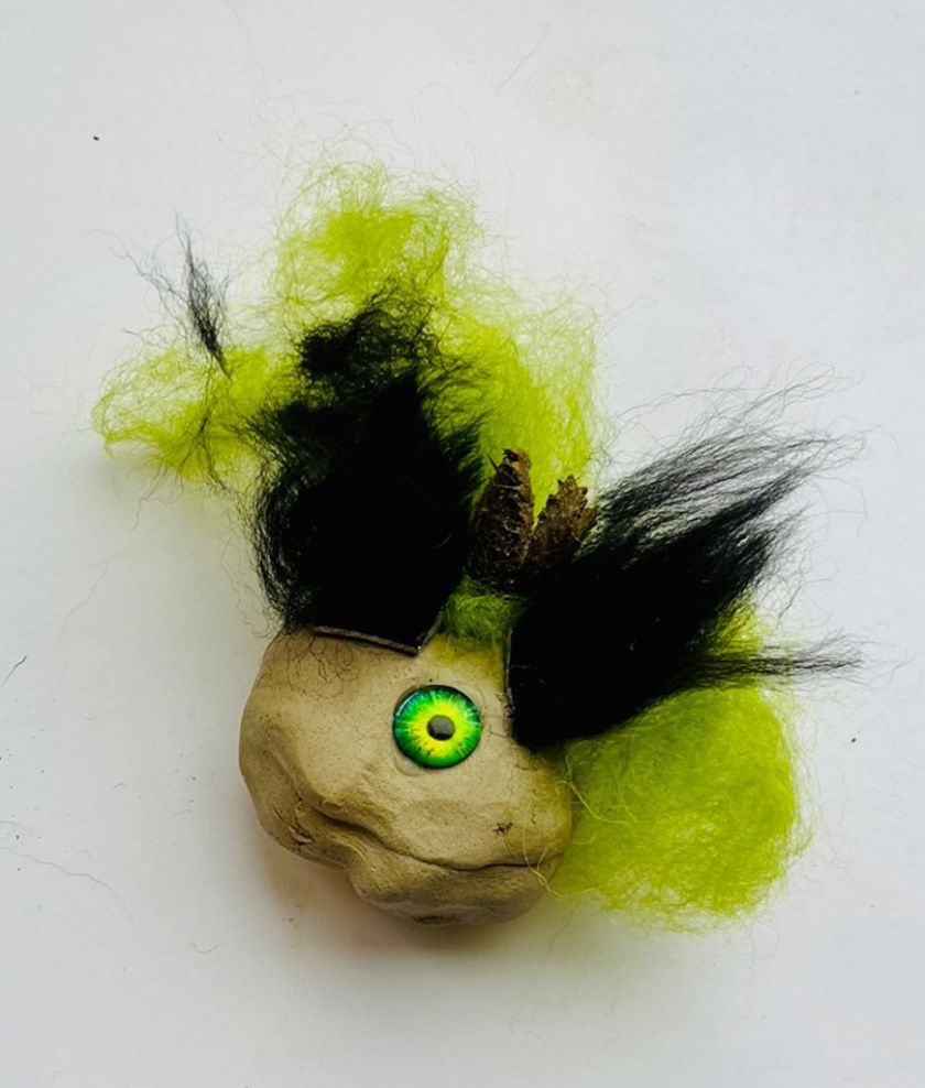 Eine gestaltete Tonkugel, kompiniert mit verschiedenen Materialien, geformt zu einen grünen Monster