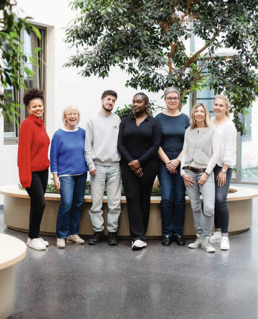 Teamfoto Inklusives Kunstprojekt, 7 Personen stehen vor einer runden Bank