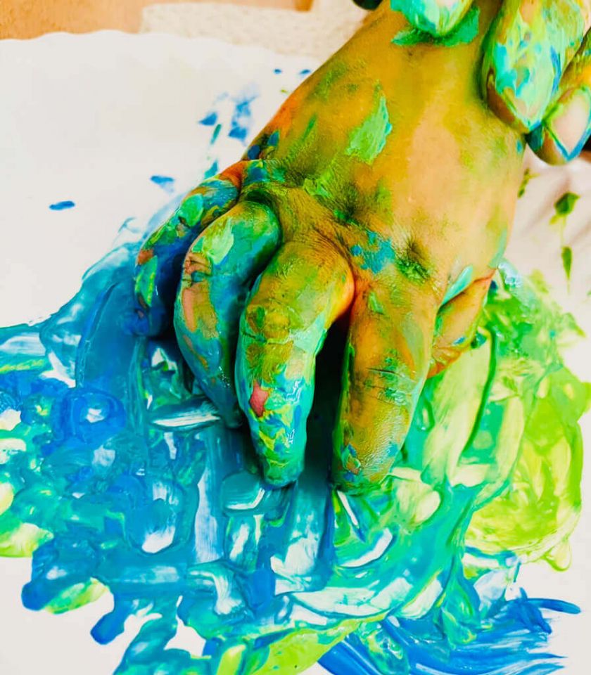 eine Kinderhand wischt bute Fraben auf ein Blatt Papier