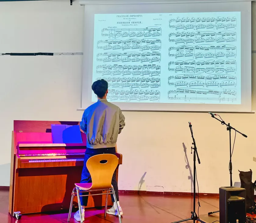 Ein Mann steht am Klavier und betrachtet eine projizierte Notenseite von Chopins „Fantasie-Impromptu“.