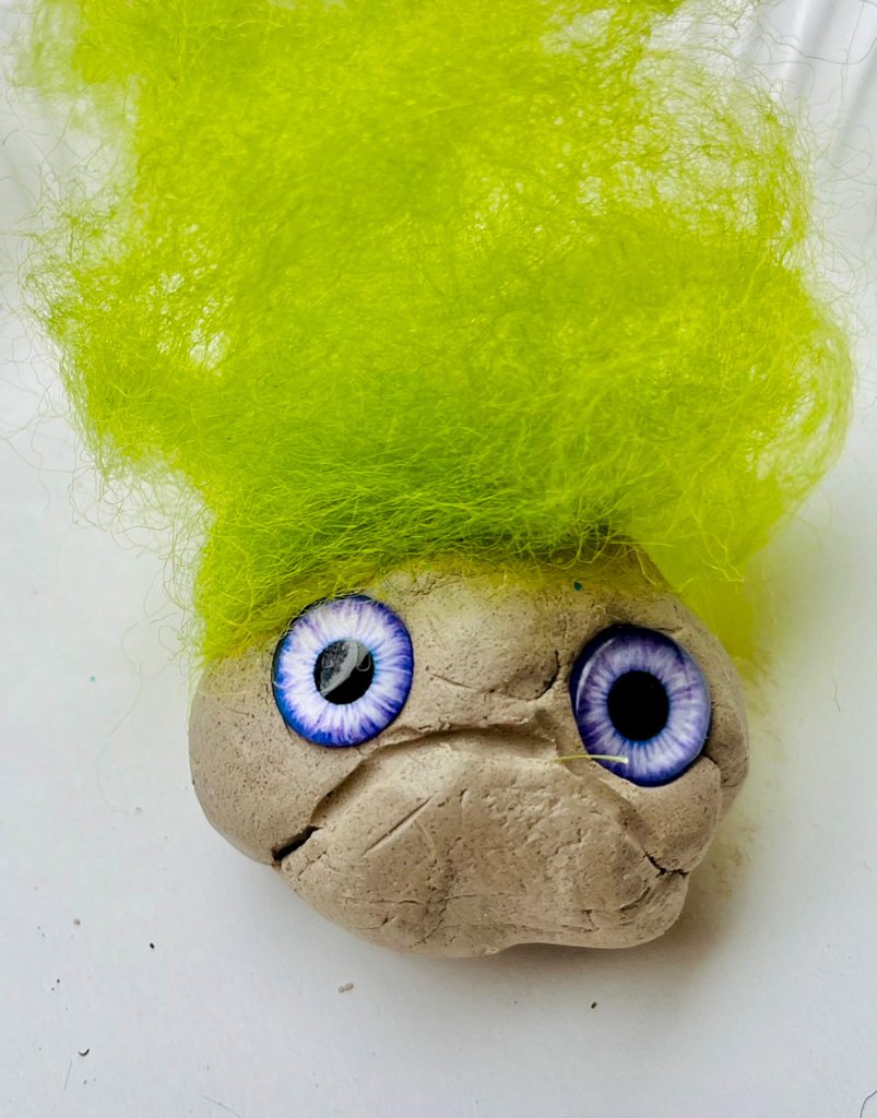 Eine gestaltete Tonkugel, kompiniert mit verschiedenen Materialien zu einen Monster mit grünen Haaren